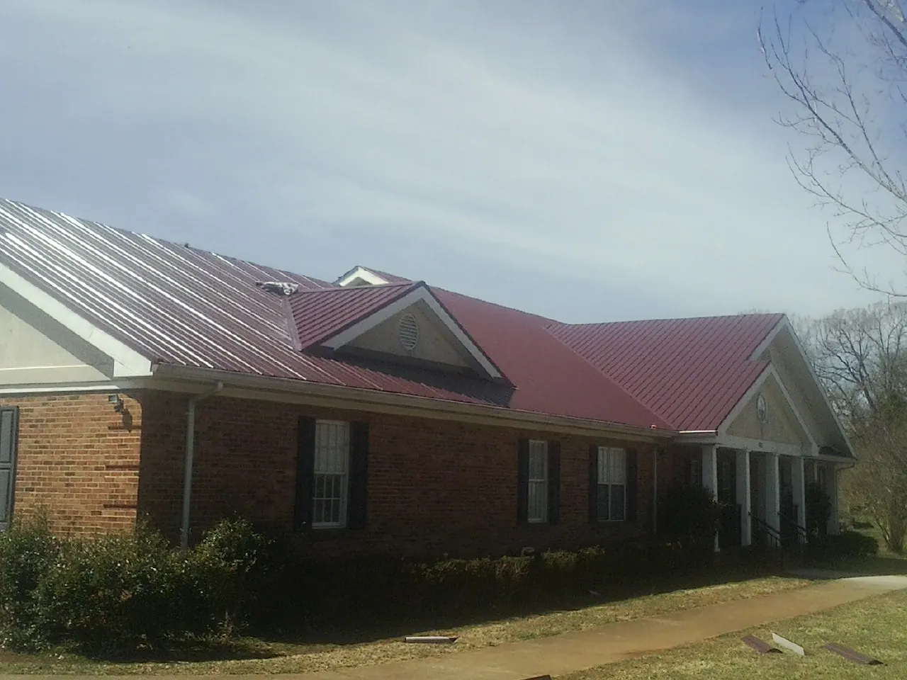 Red metal roof with gabled entries on a long brick building, from a Hail Damage Roof Repair job in Glenham