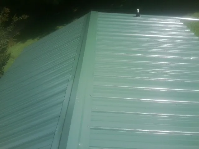 New green metal panels meeting at the ridge of a roof — Flat Roof Repair work by our crew in Glenham