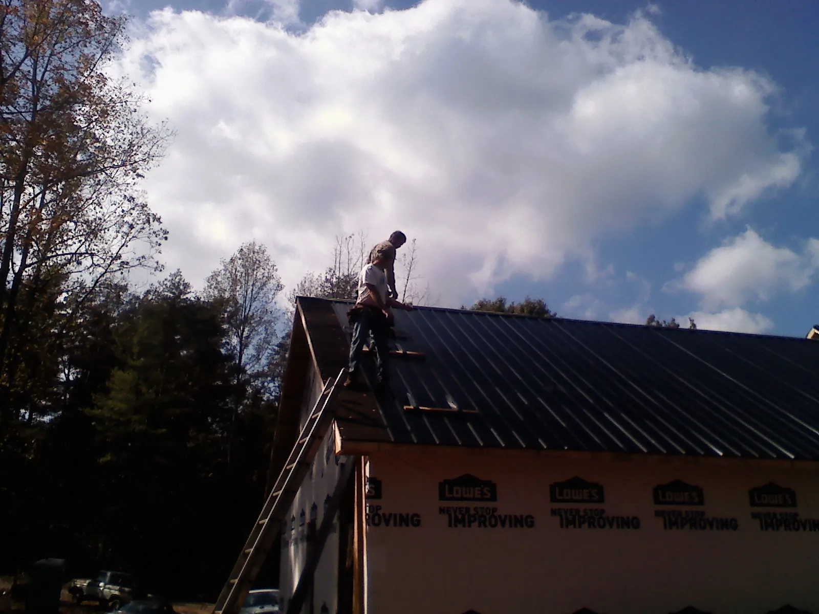 Roofer fastening dark metal panels high against a cloudy sky, from a Roof Inspection job in Glenham