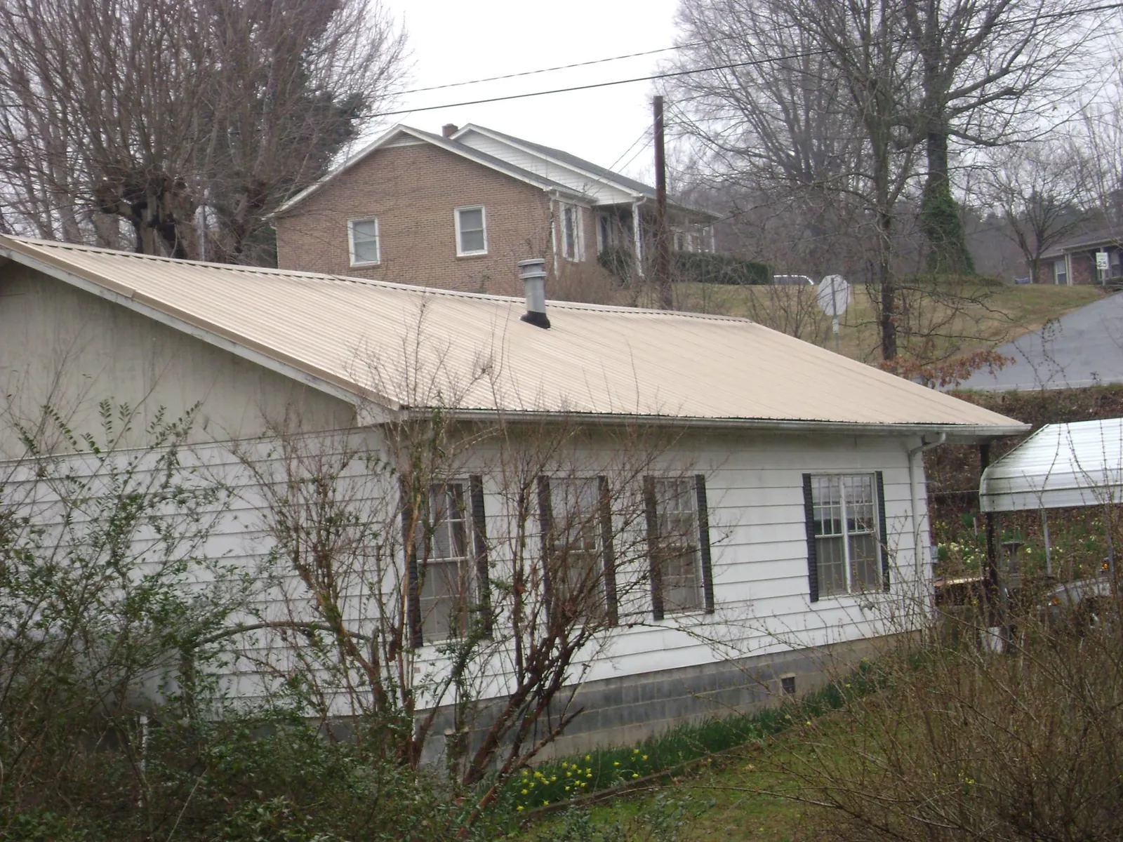 Tan metal roof on a white sided house set into a hillside — Commercial Roofing by Roofing Brothers in Glenham