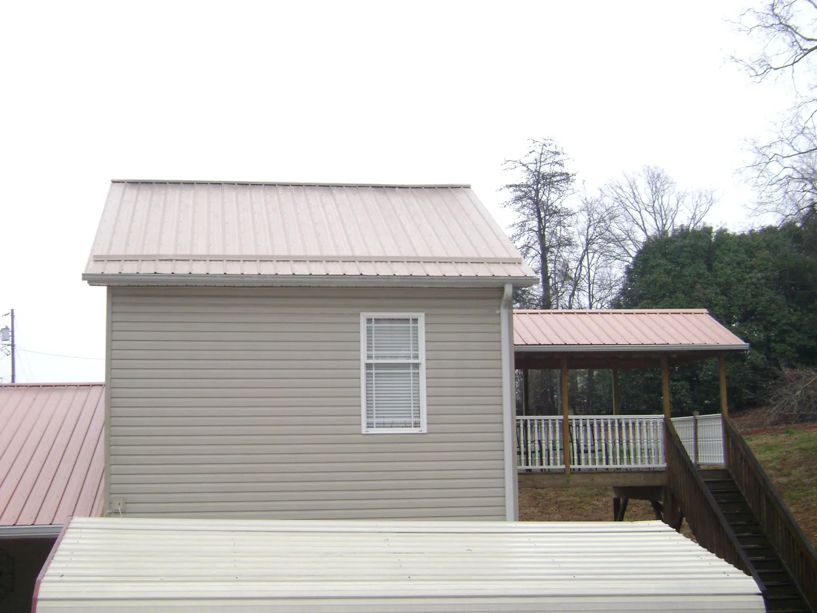 Tan metal roofs on a two story addition and attached porch, from a Roof Replacement job in Glenham